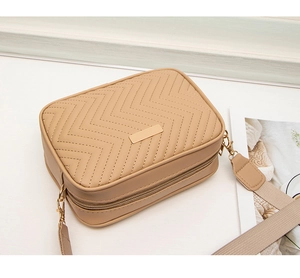 Detail of a beige crossbody camera bag featuring elegant V-shaped quilted stitching