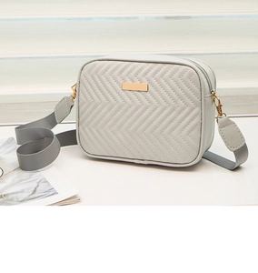 Detail of light gray square bag with chevron quilting and golden metal zipper hardware