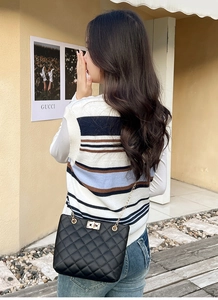 Detail shot of black quilted crossbody bag with gold lock and chain strap on a model