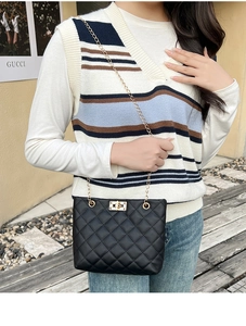 Detail of black quilted shoulder bag featuring gold chain strap and metal swivel lock