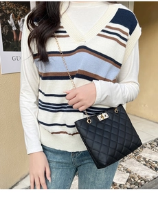 Close-up of black quilted chain bag with gold metal lock on striped knit vest