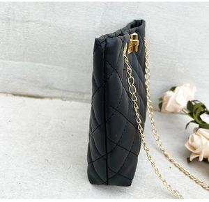 Detail view of black quilted faux leather crossbody bag with golden chain and lock