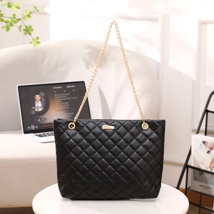 Elegante borsa a tracolla nera trapuntata con catena dorata su scrivania per estate
