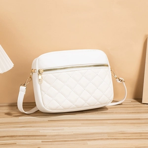Modern white quilted crossbody camera bag with gold zipper on a wooden table