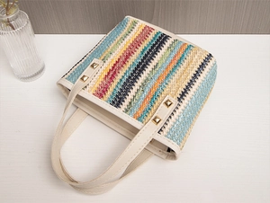 Dettaglio della borsa intrecciata arcobaleno con borchie dorate e manici bianchi