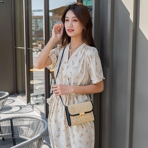 Bolso bandolera de paja tejida con ribete negro y cierre dorado en modelo con vestido