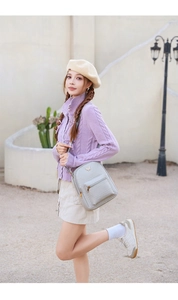 Close-up of light grey quilted backpack with golden butterfly logo worn by a model
