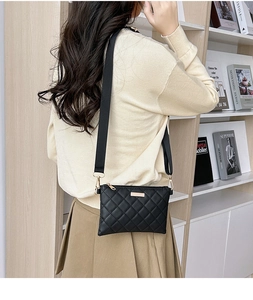Detail of black quilted crossbody bag with metal plaque and adjustable wide strap