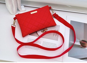 Detailed view of red quilted nylon crossbody bag with gold buckle and wide fabric strap