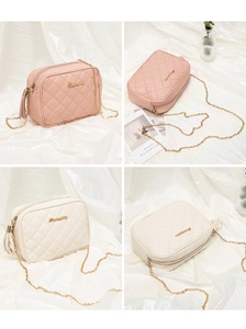 Detail of quilted crossbody bag with gold chain and stylish tassel charms in soft pink