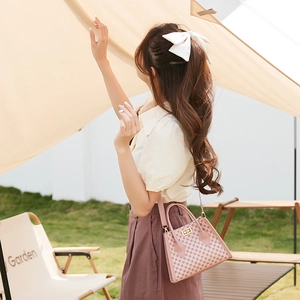 Pink printed satchel bag with metal lock shown in a stylish outdoor garden setting