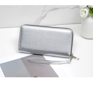 Close-up of a silver metallic long wallet with wrist strap on a modern marble surface