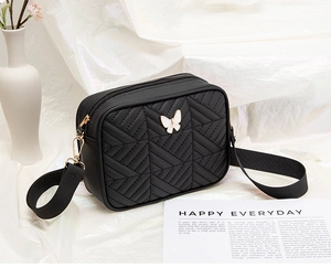 Detail of black crossbody bag featuring V-quilted pattern and white butterfly ornament