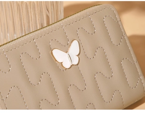 Detail of beige quilted wallet with wave stitching and a gold butterfly ornament
