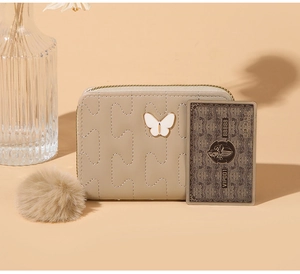 Detail of beige quilted wallet featuring a butterfly metal ornament and a soft pom-pom charm