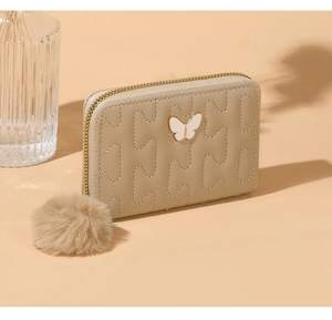 Detail of beige quilted faux leather wallet with gold butterfly and plush pompom charm