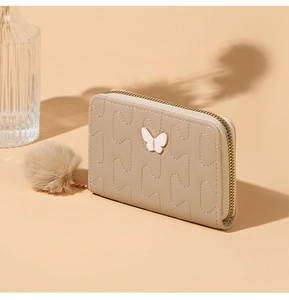 Detail of beige quilted leather wallet with white butterfly hardware and pompom charm