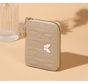 Detail of light beige quilted wallet with butterfly metal charm and plush pompom keychain