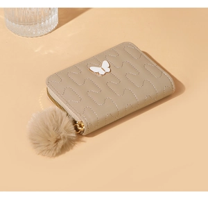 Close-up of beige quilted PU leather wallet with butterfly clasp and plush pompom charm