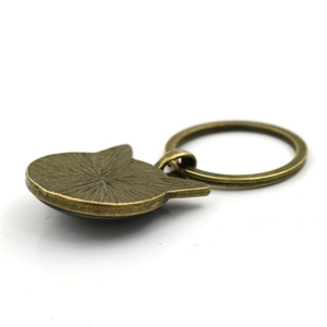 Vista trasera de un llavero de gato en bronce con textura radial y anillo de metal