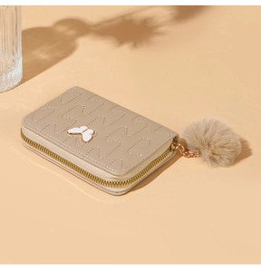 Close-up of beige quilted card holder with golden zipper, butterfly detail and fur pompom