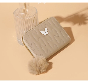 Detail of beige quilted wallet with butterfly metal logo and soft faux fur pompom charm