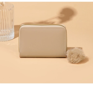 Detail view of cream puzzle-stitched coin purse with a soft faux fur pompom keychain
