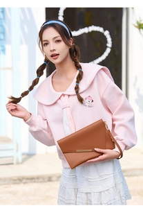 Dettaglio di una pochette a busta in pelle marrone con felpa rosa a tema orso