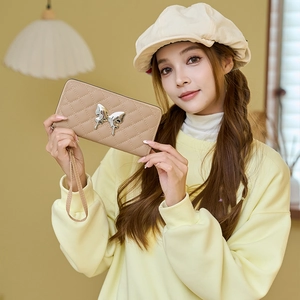 Quilted khaki long wallet with silver butterfly ornament and wrist strap shown by model