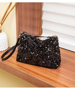 Close-up of black sequin baguette bag with gold zipper detail on a rustic wooden table