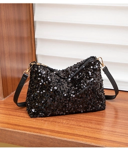 Detail of black sequined shoulder bag with golden metal hooks on wooden shelf
