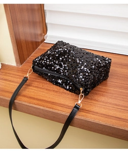 Macro detail of black sequin fabric with gold zipper and leather strap on a shoulder bag