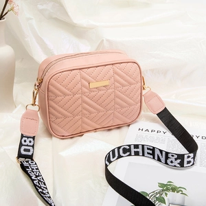 Pink quilted crossbody camera bag with wide woven strap and gold hardware on white cloth