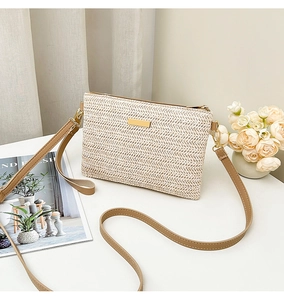 Detail of hand-woven straw crossbody bag with gold metal plate and brown faux leather strap