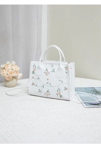 Detailed view of floral embroidery on a white square crossbody bag with round handles