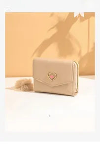 Detail of beige short wallet with heart buckle and fur ball charm on a warm background
