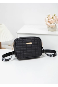 Detail of black quilted crossbody bag with golden metal plate and jacquard wide strap