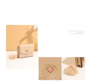 Detail view of beige tri-fold short wallet with heart hardware and plush pompom charm