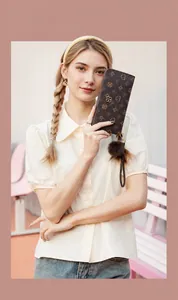 Close-up of brown floral patterned wallet with plush pom-pom and wrist strap held by model