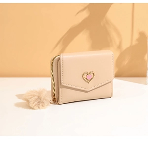 Detail of cream trifold wallet featuring a gold heart clasp and soft fur ball charm