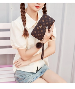 Close-up of long zip wallet with vintage floral pattern, wrist strap and plush pompom charm