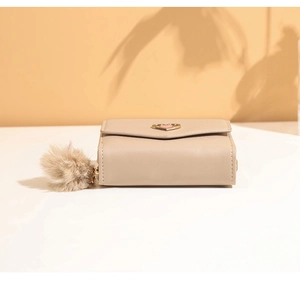 Close-up of beige short tri-fold wallet with gold heart buckle and brown pompom charm