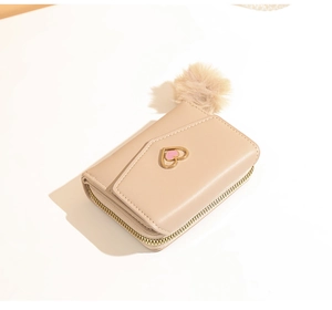 Detail of beige faux leather wallet featuring a gold heart clasp and soft fur pompom charm
