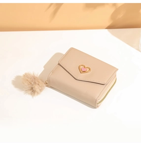 Close-up of beige short leather wallet with gold heart buckle and pompom zipper detail