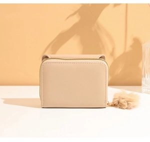 Close-up of beige faux leather mini wallet with gold zipper and plush ball charm