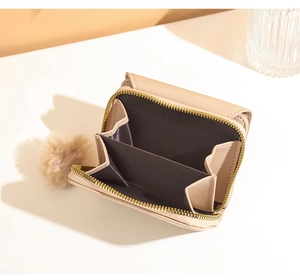 Detail of beige faux leather wallet with gold zipper and a cute pompom keychain accessory