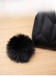 Dettaglio del portafoglio in pelle trapuntata nera con pompon in ecopelliccia e cuciture fini