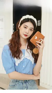 Brown oil skin short wallet with butterfly ornament and plush ball held by model