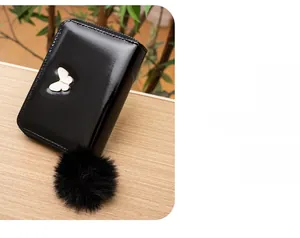 Detail of black patent leather wallet featuring butterfly ornament and soft faux fur pompom