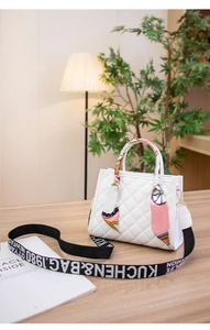 Close-up of quilted white handbag featuring decorative scarf handle and wide woven strap